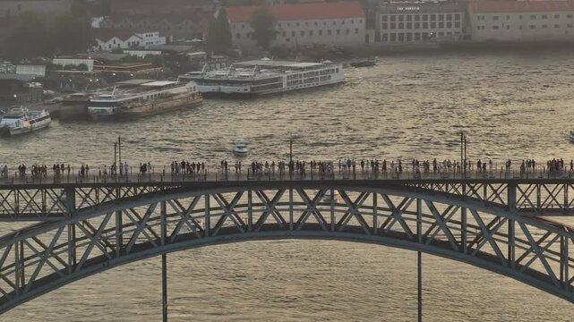 Aerial view of the Dom Luis I Bridge over the Douro River with pedestrians walking on the upper deck and river cruise boats below in Porto, Porto District, Portugal.
