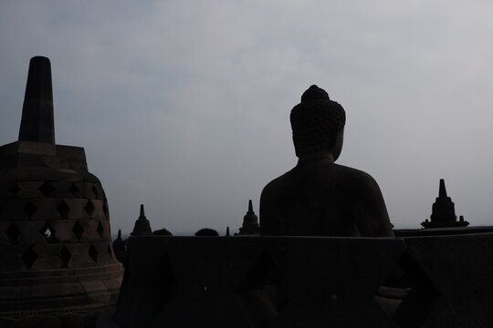 Silhouette of Seated Buddha Statue and Stupa Against Overcast Sky at Borobudur Temple