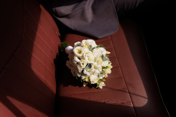 Obraz premium White rose bouquet rests on a red leather car seat