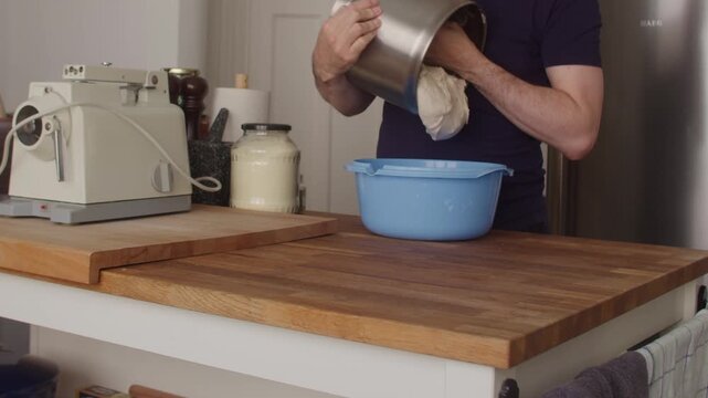 Emptying kneaded bread dough from mixing bowl into blue bowl for bulk proofing