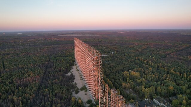 Aerial view of the massive Duga radar array rising above the dense forest landscape during golden hour in Ivankivs'kyi district, Kyiv Oblast, Ukraine.