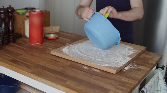 Emptying bread dough onto floured cutting board on wooden kitchen island worktop