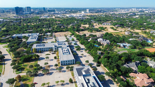 Rooftop solar arrays line commercial tech centers adjacent to Stonebriar Creek Estates. Office properties transition into wooded suburban residential developments, Frisco, Texas
