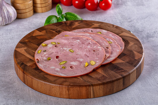 Sliced mortadella with pistachios on wooden cutting board, fresh basil and cherry tomatoes background
