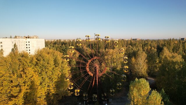 Aerial view of the abandoned Ferris wheel in the amusement park of Pripyat, surrounded by overgrown autumn trees and decaying Soviet-era buildings in Pripyat, Kyiv Oblast, Ukraine.