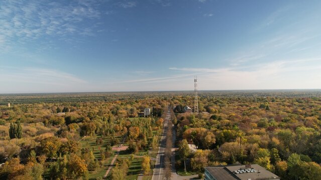 Aerial view of the Chornobyl exclusion zone with its iconic communication tower, a long road cutting through dense autumn forests, and scattered buildings in Chornobyl, Kyiv Oblast, Ukraine.