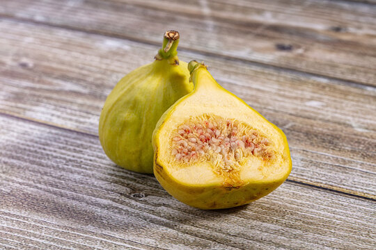 Fresh figs on rustic wooden surface, one cut open to show pinkish seeds and yellow flesh