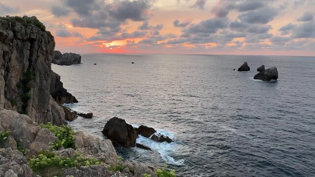 Typical summer sunset on the Atlantic coast, with salmon-pink tones in the sky, calm gray ocean water and massive rocky cliffs.