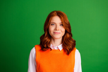 Fototapeta premium Smiling redhead woman portrait in orange sweater against green background, casual studio headshot conveying warmth, confidence and contemporary fashion