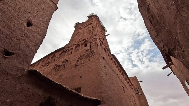 Eroded earthen tower of the Ait Benhaddou ksar seen from below, Ouarzazate, Morocco, bright cloudy sky