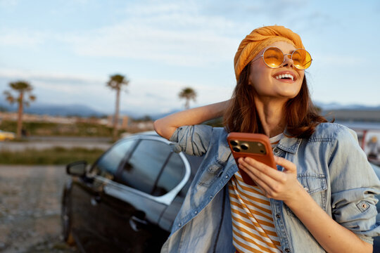 Woman enjoying outdoor lifestyle, smiling beside a car, wearing striped shirt and denim jacket, sunglasses, casual travel mood, candid roadside portrait.
