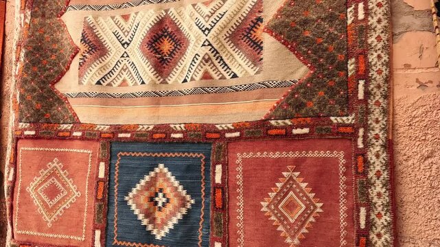 Handwoven Berber wool rugs with diamond motifs displayed on a medina wall, Marrakech, Morocco, daylight