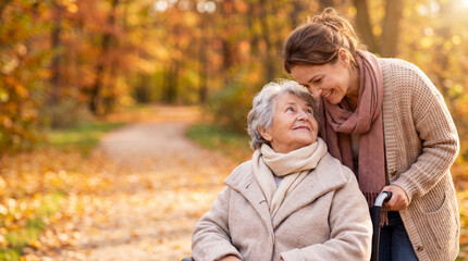 Fototapeta premium Elderly woman in wheelchair smiles at caregiver in autumn park, surrounded by colorful foliage and a winding path in the background