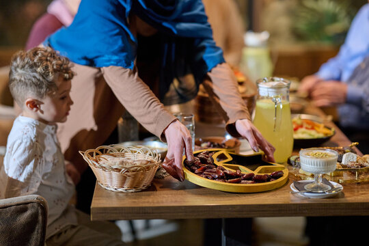 Family Gathering at Dinner Table With Woman in Headscarf Serving Dates to Child