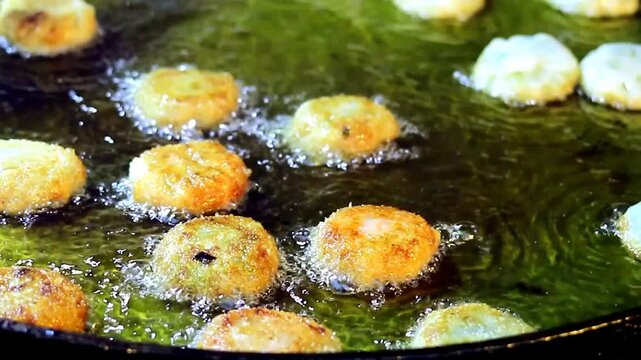 Street food vendor flips fried Chinese chive dumplings with stainless steel tongs in bubbling hot oil at a night market food stall, small business street food service in Thailand
