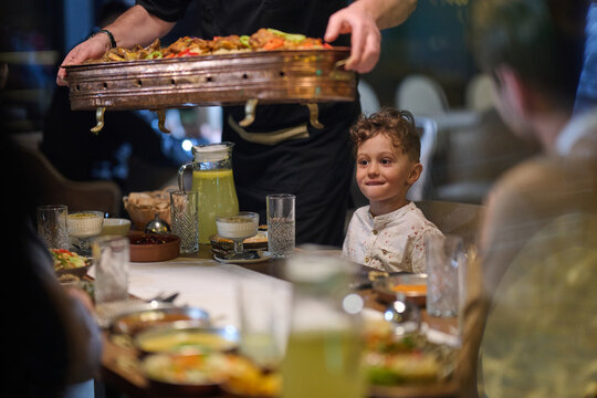Happy Child Waiting at Family Dinner As Server Brings Large Tray of Food in Restaurant
