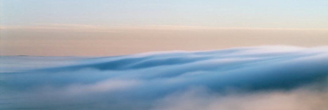 Rolling fog over calm water under soft pastel sky
