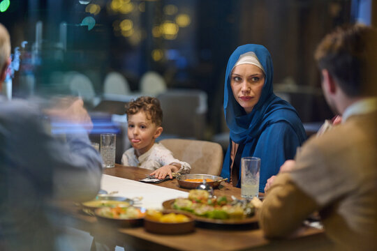 Woman Wearing Hijab and Young Boy Sharing Family Dinner at Restaurant Table in Evening
