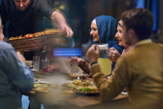 Family Dinner Celebration With Woman in Headscarf Sharing Food and Drinks at Restaurant Table