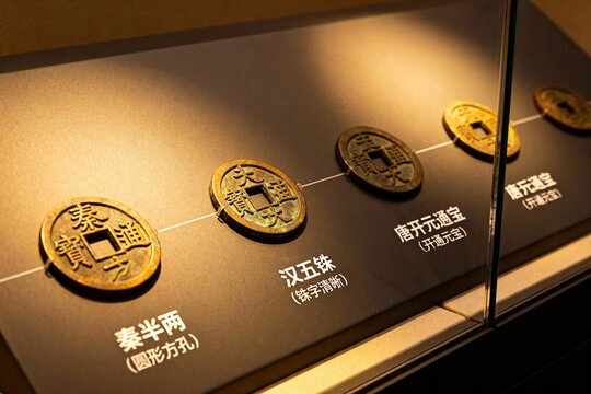 Ancient Chinese coins displayed in a museum exhibit, including Qin Banliang, Han Wu Zhu, and Tang Kaiyuan Tongbao.