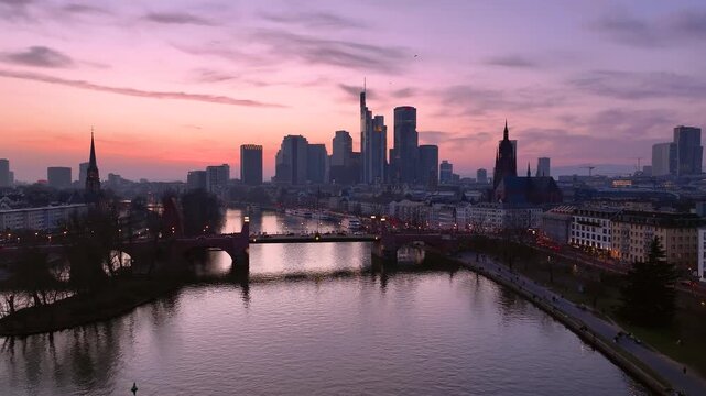 Aerial view of alte Brucke spanning the Main River with the illuminated Frankfurt skyline at sunset in Frankfurt am Main, Hessen, Germany.