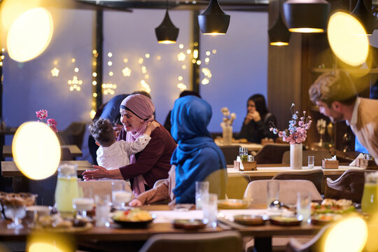Multigenerational Muslim Family Sharing Warm Dinner Celebration in Restaurant With Baby and Hijab