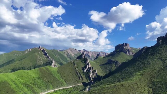 Slow ascending aerial drone view of rugged mountain range along Rock Road to Zhagana, Gannan Gansu, bright blue sky with fluffy white summer clouds