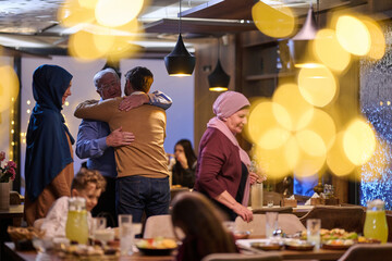 Naklejka premium Multi-Generational Muslim Family Hugging at Festive Dinner Reunion With Warm Lights and Food