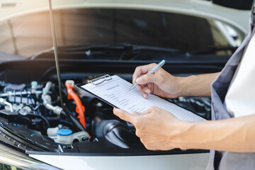 Obraz premium Auto check up and car service shop concept. Mechanic writing job checklist to clipboard to estimate repair quotation to client at workshop garage.