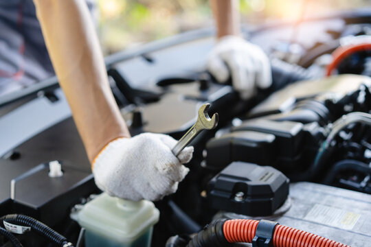Mechanic technician hands holding wrench tools repairing car engine under the hood in auto repair garage