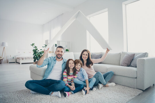 Happy family sitting under a cardboard roof in a bright living room celebrating new home, security and togetherness