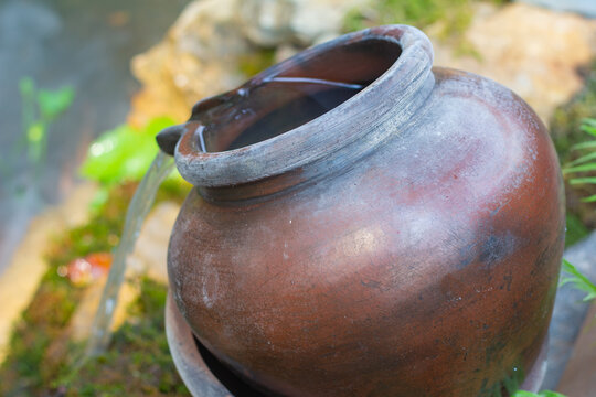 Close up of a vintage clay pot water fountain with flowing water in a tropical garden setting.