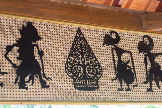 Black silhouette of traditional Indonesian Wayang Kulit shadow puppets mounted on a rattan woven background