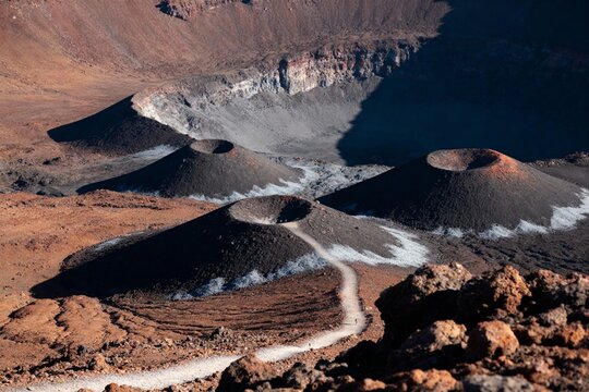 Volcanic landscape featuring multiple cinder cones and a large caldera with rugged terrain and winding path