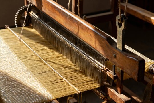 Close-up of a traditional wooden loom in operation, weaving fabric with visible threads and mechanical components.