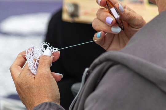 Hands creating white handmade tatting lace