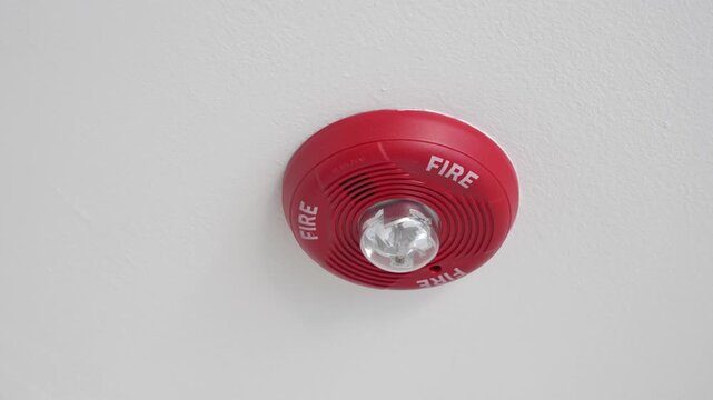 flashing fire alarm detector on a white ceiling, indicating an active emergency warning video. Fire safety and smoke detection concept for home, office, building security and emergency preparedness