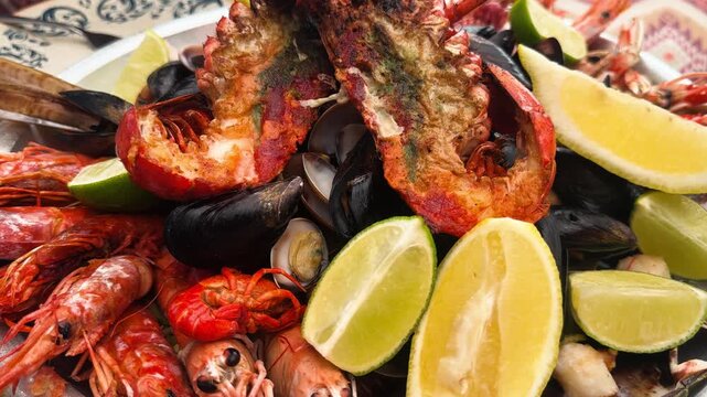 Grilled seafood platter with shrimp, lobster and mussels garnished with lime wedges served on a plate. High quality 4k footage