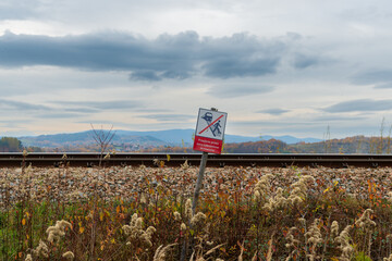 Railway no trespassing warning sign beside an active track near Jezioro Mucharskie. Rail safety concept with ballast, autumn vegetation and mountain landscape, suitable for transportation safety, dang © Volha