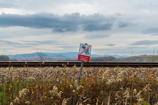 Railway no trespassing warning sign beside an active track near Jezioro Mucharskie. Rail safety concept with ballast, autumn vegetation and mountain landscape, suitable for transportation safety, dang