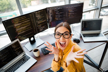 Happy female programmer celebrating a coding breakthrough at a multi-monitor workstation in a...