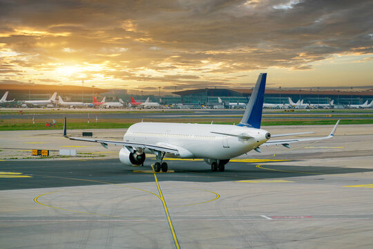 Large commercial jet taxiing along the tarmac at an airport as the sun sets behind the terminal buildings during the quiet evening hours