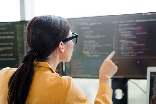 Female software developer pointing at code on a large computer screen in an office while reviewing and debugging software