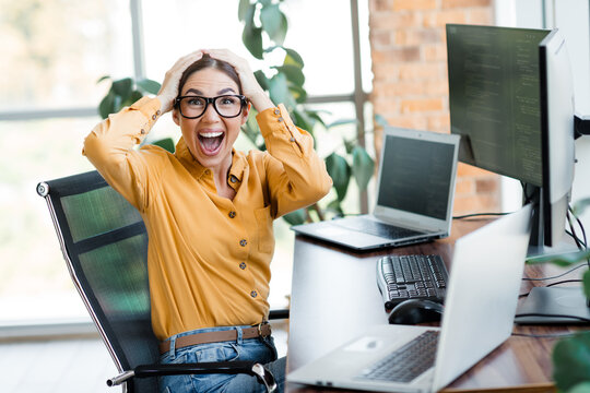 Excited female programmer celebrating a project success at her desk with laptops and monitors in a bright modern office
