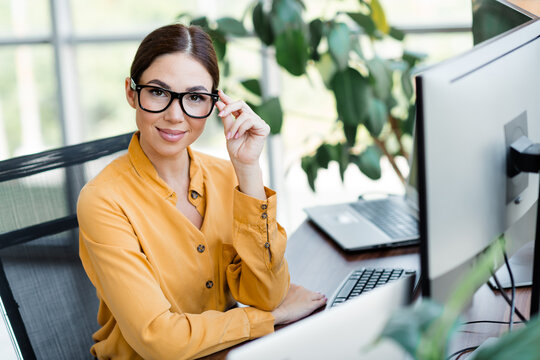 Businesswoman in glasses smiling confidently while working at computer in a modern bright office with plants and natural light