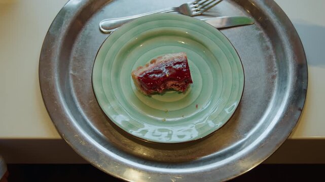 Close up of hand placing and adjusting pieces of pie on green ceramic plate with spiral pattern set within larger metal tray. Fork visible beside food as person interacts with dessert