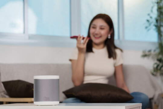 Smart speaker voice assistant on coffee table with Asian woman using smartphone in background