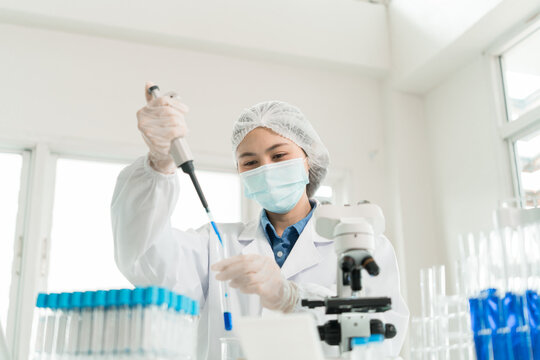 Female Laboratory Scientist Analyzing Samples with Pipette, Microscope and Laptop in Modern Research Laboratory