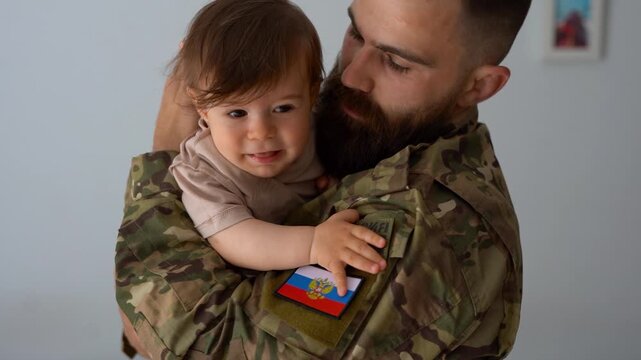 Russian male soldier in military uniform returning home to family - Father hugging baby son - Emotional homecoming, happiness and love concept	