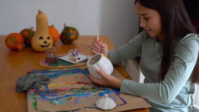 Young girl painting on a pumpking cup during fall season for Halloween event - Holiday, childhood and autumn lifestyle concept	